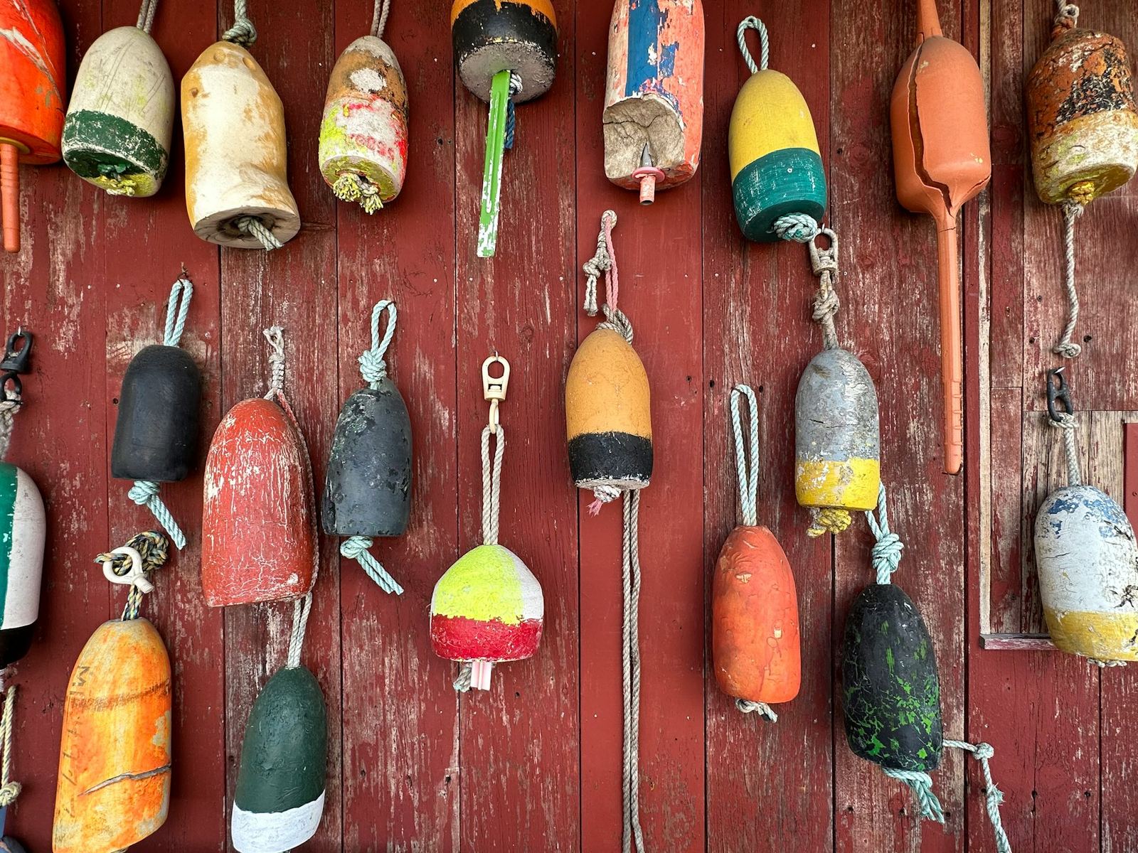 Wall of painted lobster buoys in red, yellow, green and orange on red clapboard