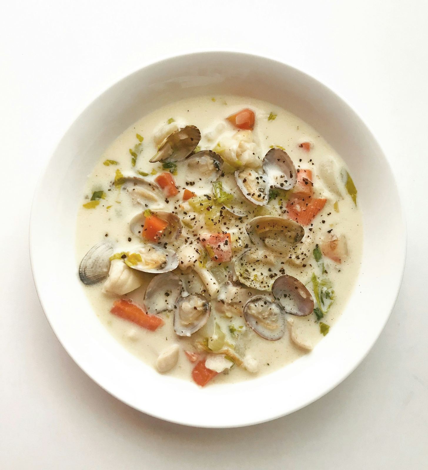 White bowl of creamy clam chowder with whole clams, carrot and herbs