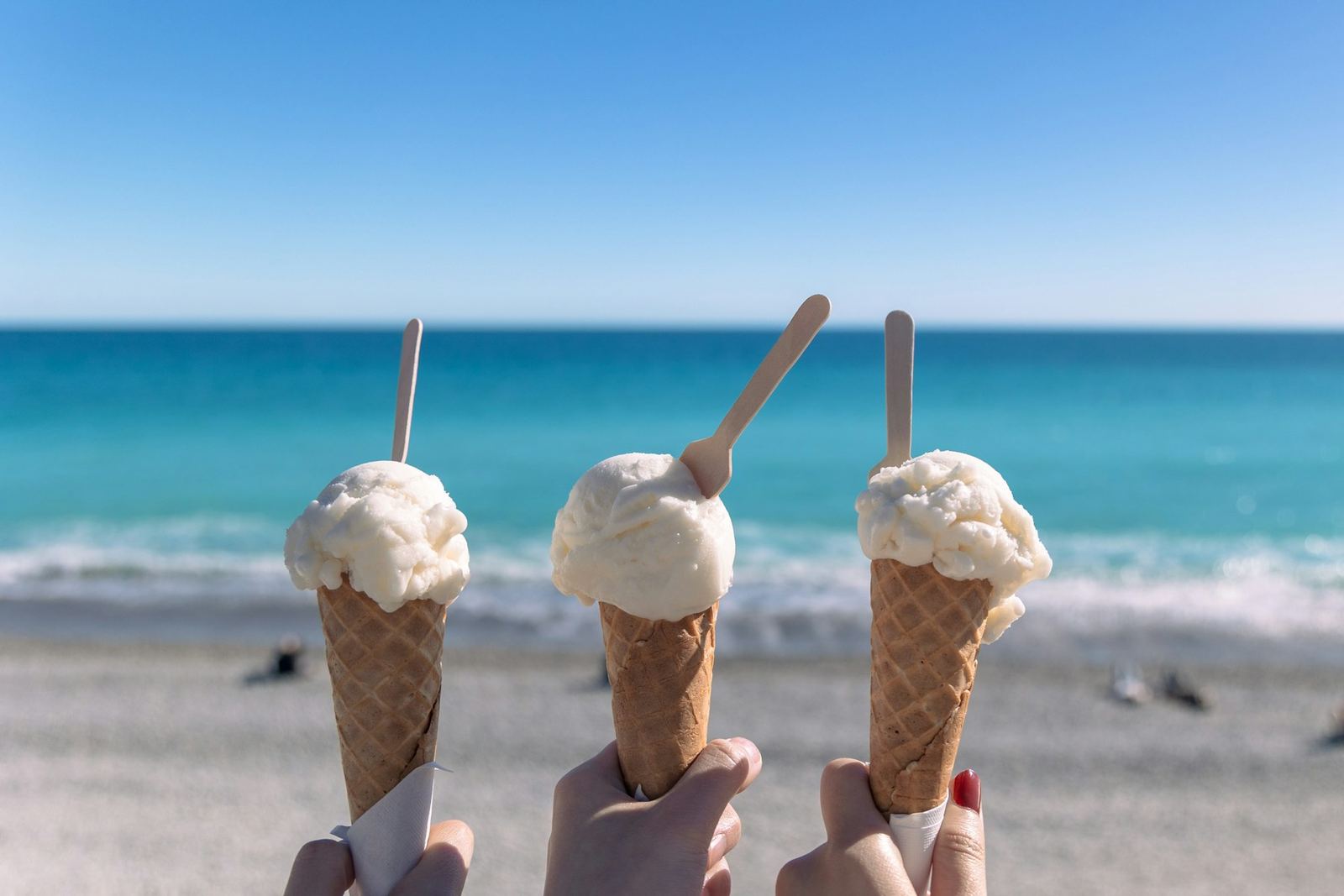 Three soft-serve cones held up in front of the ocean