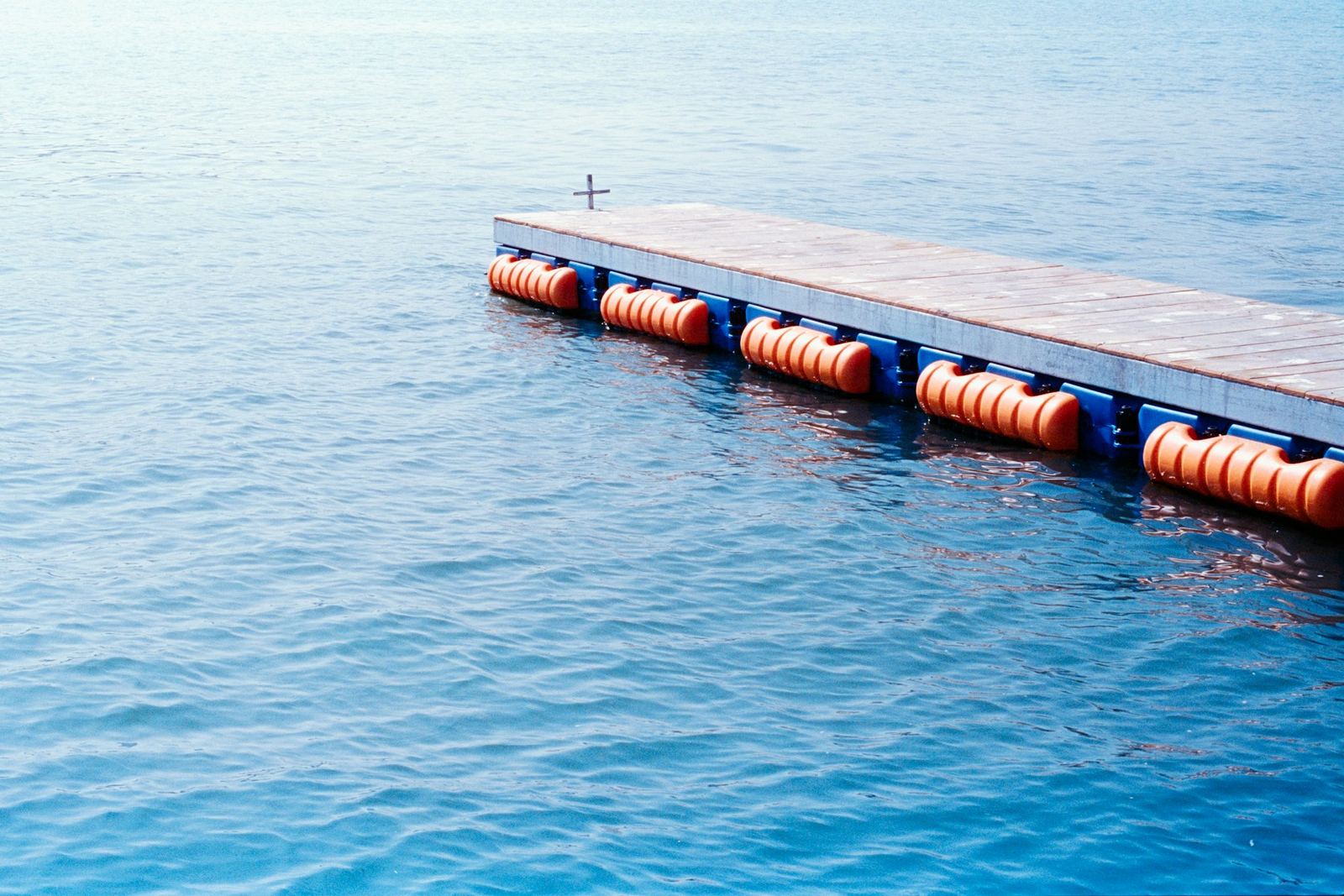 A floating dock with orange buoys on calm blue water