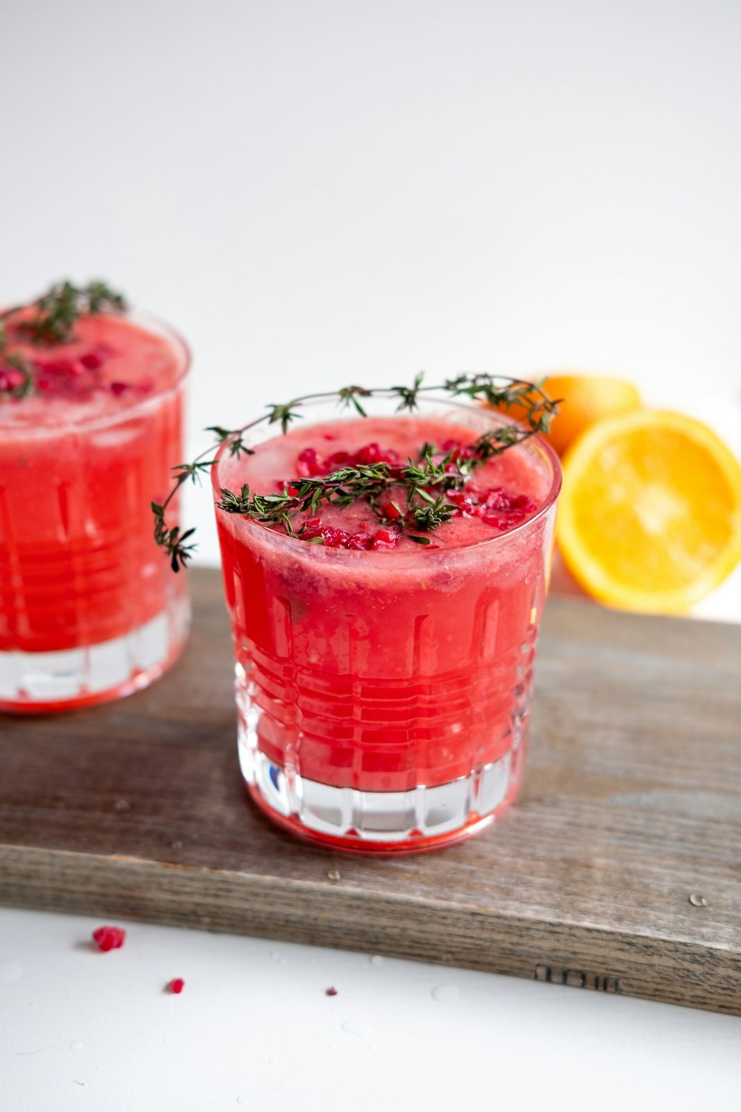 Two glasses of red strawberry lemonade with a thyme sprig on a wooden board