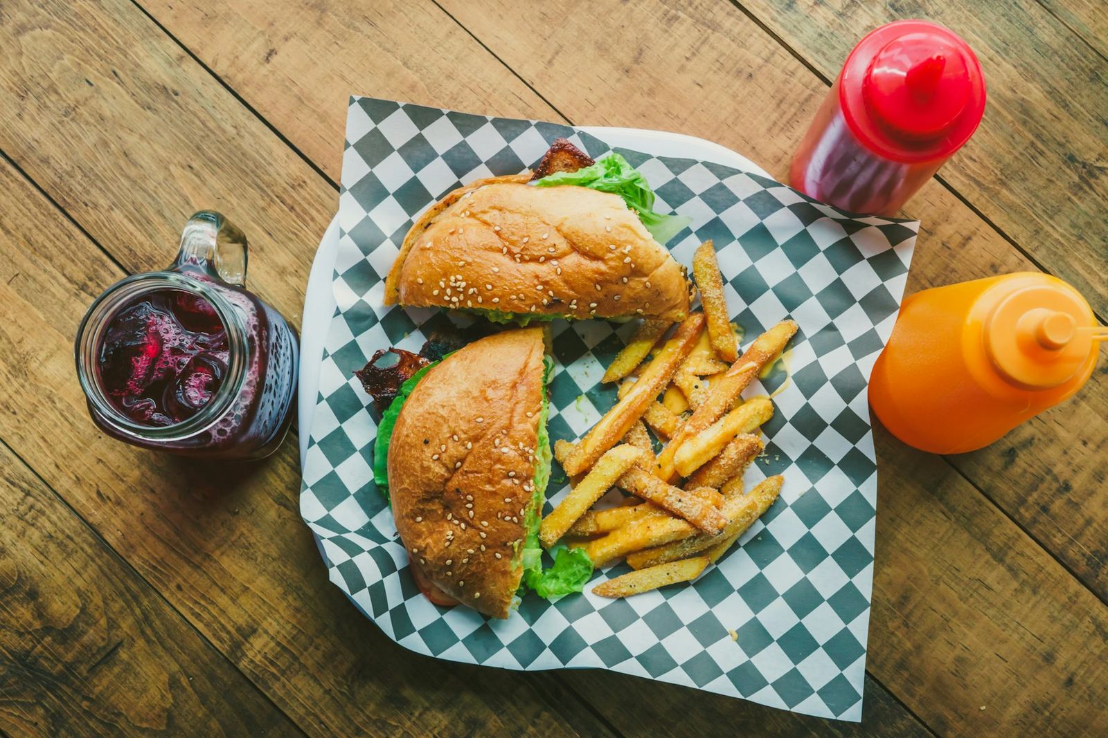 Haddock sandwich and fries on green checkered paper, with ketchup and mustard bottles and a berry drink