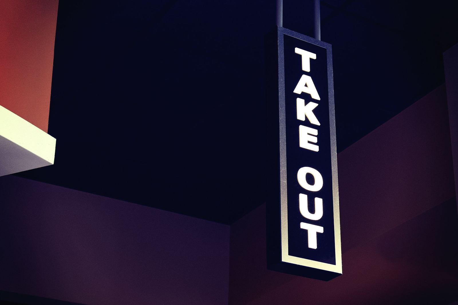 A vertical TAKE OUT sign glowing against a dark blue sky